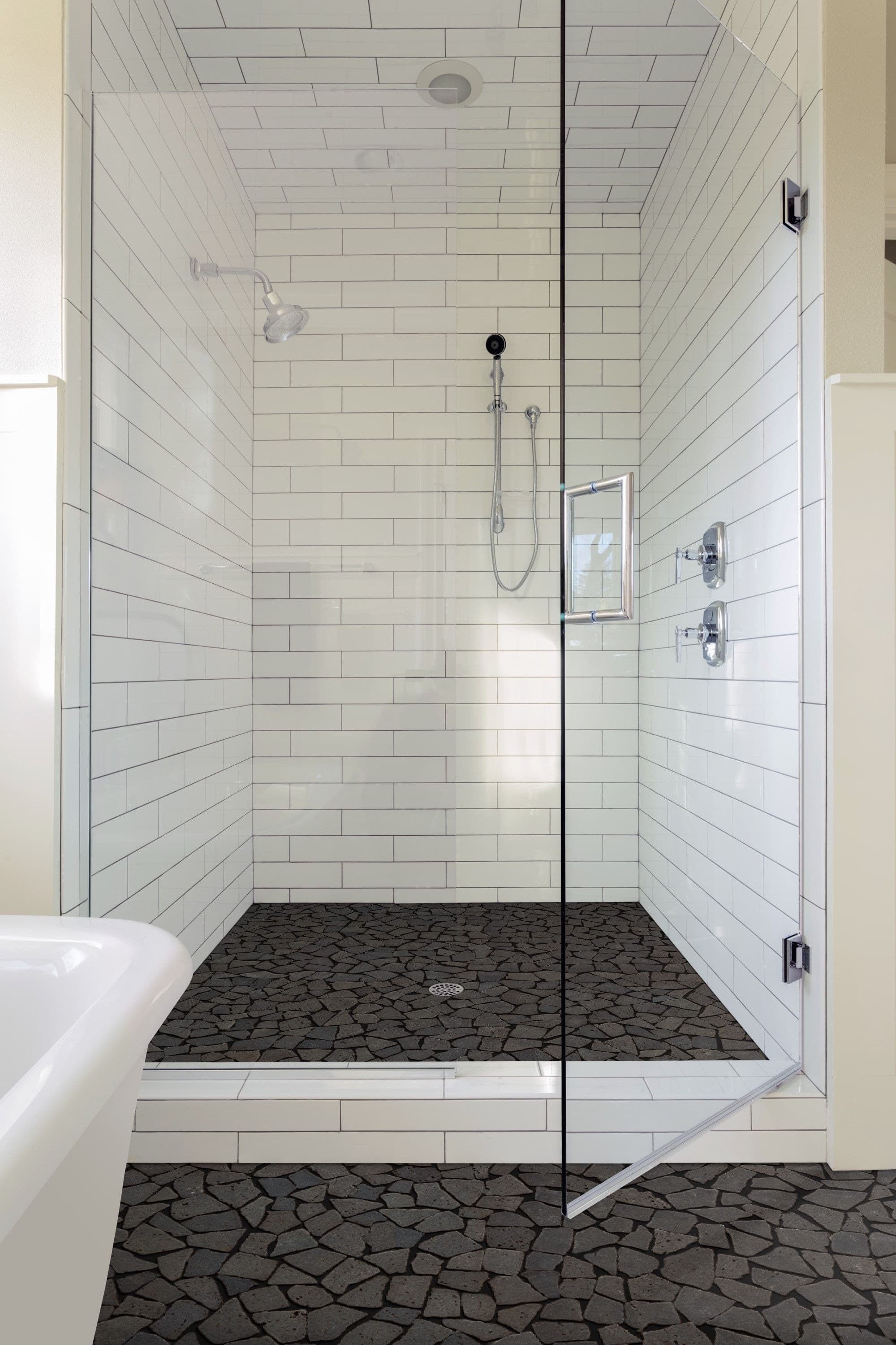 White subway tile shower with dark pebble-style floor tile