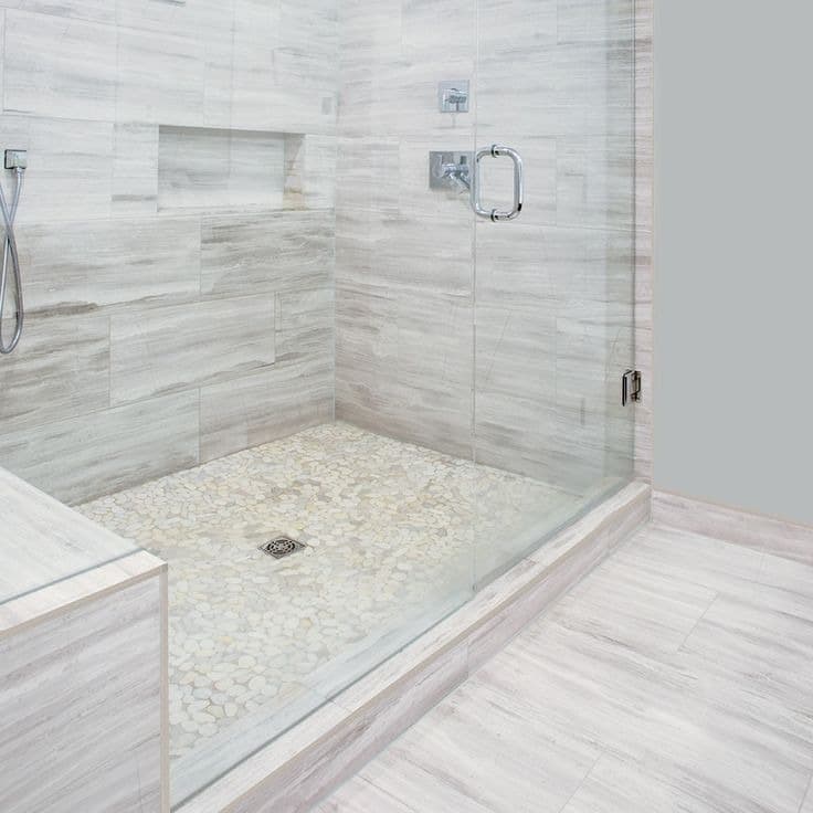Glass-enclosed walk-in shower with marble-look tile and pebble floor